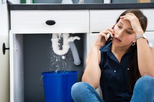upset woman on phone near leaking sink.